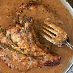 a pan filled with meat and gravy on top of a wooden table next to a fork