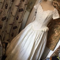 a white wedding dress sitting on top of a mannequin next to a curtain