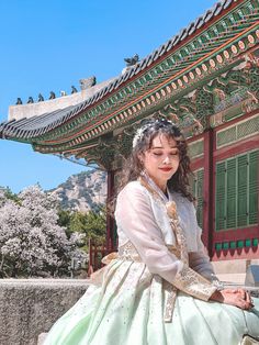 a woman in a white and green dress sitting on a stone wall next to a building