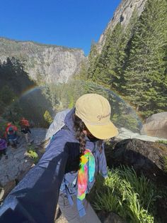 a person with a hat and backpack is looking at a rainbow in the sky above them