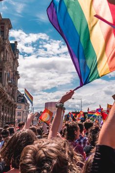 a group of people holding rainbow flags in the air at a pride parade on a sunny day