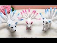 three white and blue toy animals sitting on top of a table next to a pink rose