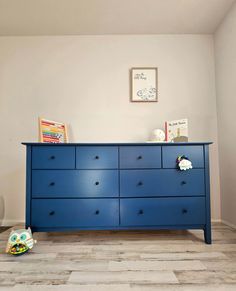 a blue dresser sitting on top of a hard wood floor next to a white wall