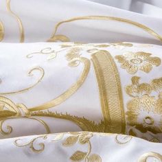 white and gold bedding with floral designs on it's edges, including one pillow