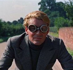 a man riding a bike down a street with large goggles on his face and wearing a suit