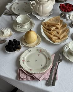 a table topped with plates and cups filled with desserts next to silverware on top of a white table cloth