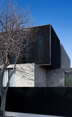 the building is made out of black bricks and has a tree in front of it