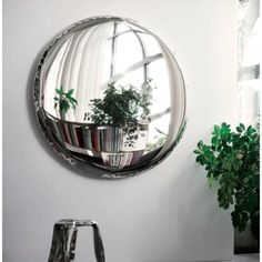 a round mirror hanging on the wall next to a potted plant