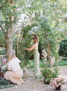 two women are working on an outdoor wedding ceremony in the garden with flowers and greenery