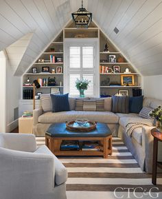 a living room filled with furniture and bookshelves under a slanted ceiling over a striped rug