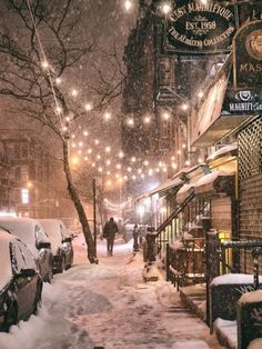 a city street covered in snow at night with people walking on the sidewalk and parked cars