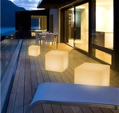 an outdoor deck with lights on it and chairs around the table, overlooking the water