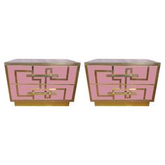 a pair of pink and gold nightstands with metal handles on each side, one has an intricate design in the middle