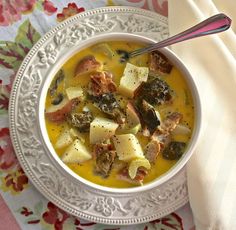 a white bowl filled with soup on top of a floral table cloth next to a spoon