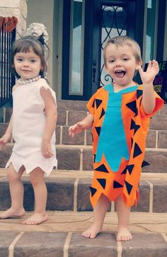 two young children dressed up in costumes standing on steps outside a house with their hands in the air