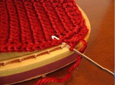 a close up of a red knitted cushion with a needle in the middle and yarn on top