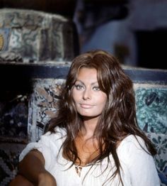 a woman with long hair sitting in front of a chair and looking at the camera