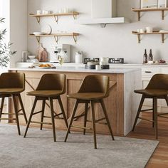 three wooden stools sit in front of an island with white countertops and open shelving