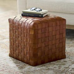 a brown leather ottoman with a book on top and glasses sitting on top of it