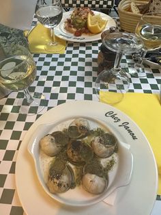 a white plate topped with oysters on top of a checkered table cloth next to wine glasses