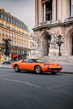 an orange sports car is parked on the side of the road in front of some buildings