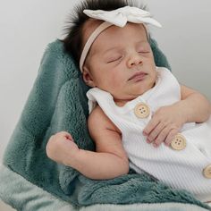 a baby wrapped in a blanket sleeping on top of a green blanket with buttons and a white headband