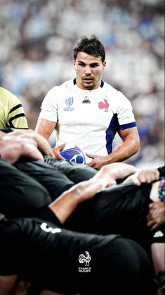 a rugby player holding the ball in his hands while others watch from the sidelines