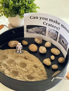 a toy astronaut standing next to some rocks in a pan with a sign on it