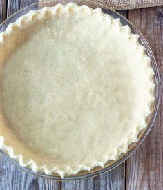 an uncooked pie crust in a glass dish on a wooden table with a burlcloth