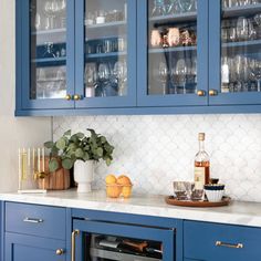 a kitchen with blue cabinets and marble counter tops, wine glasses on the cabinet doors