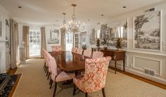 a dining room table with pink chairs and pictures on the wall in front of it