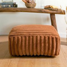 a brown ottoman sitting on top of a hard wood floor next to a wooden table