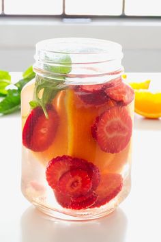 a mason jar filled with sliced strawberries and oranges on top of a table