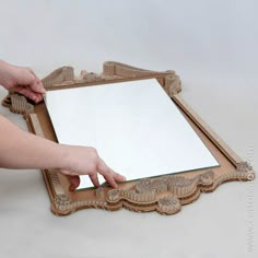 a person holding a mirror on top of a wooden frame with an ornate pattern and border