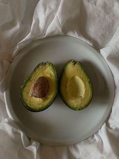 an avocado cut in half on a plate with white linens behind it