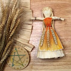 a paper doll next to some wheat stalks and a pentagramle on a wooden table