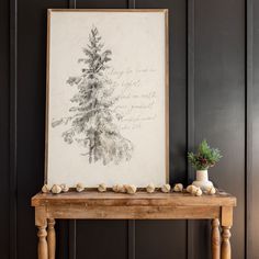 a wooden table sitting next to a painting and vase on top of it in front of a black wall