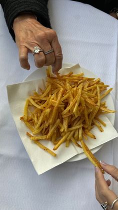 two hands reaching for french fries on a plate