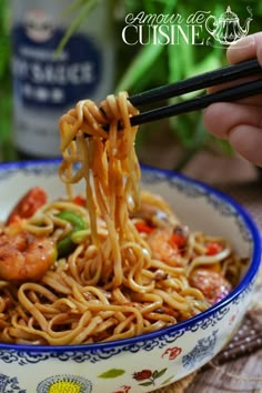 someone is holding chopsticks over noodles in a bowl with shrimp and vegetables on it