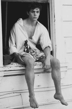 black and white photograph of man sitting on window sill