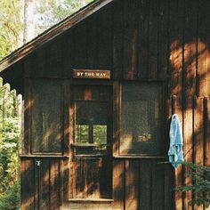 an old wooden building in the woods with a blue umbrella hanging from it's side