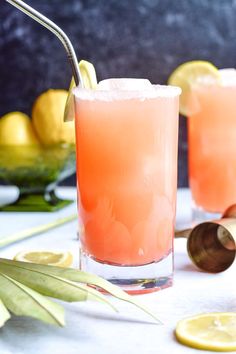 two glasses filled with lemonade sitting on top of a table next to sliced lemons