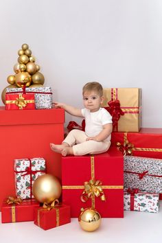 a baby sitting on top of boxes with christmas presents around it and gold balls in the background