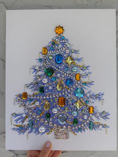 a hand holding up a card with a christmas tree made out of beads and jewels