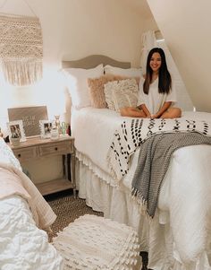 a woman sitting on top of a white bed in a bedroom next to a dresser