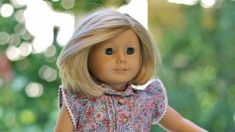 a close up of a doll with blonde hair and blue eyes, wearing a dress