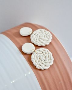 two white flower shaped earrings sitting on top of a pink and white vase with gold accents