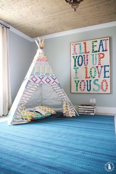 a teepee tent sitting on top of a blue rug next to a wall hanging