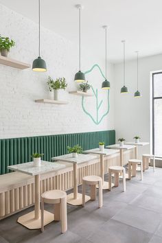 the interior of a restaurant with tables and stools, potted plants on the wall