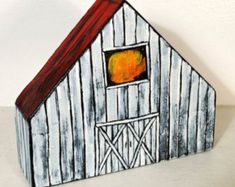 a painted wooden barn with a red roof and window on the side, in front of a white wall